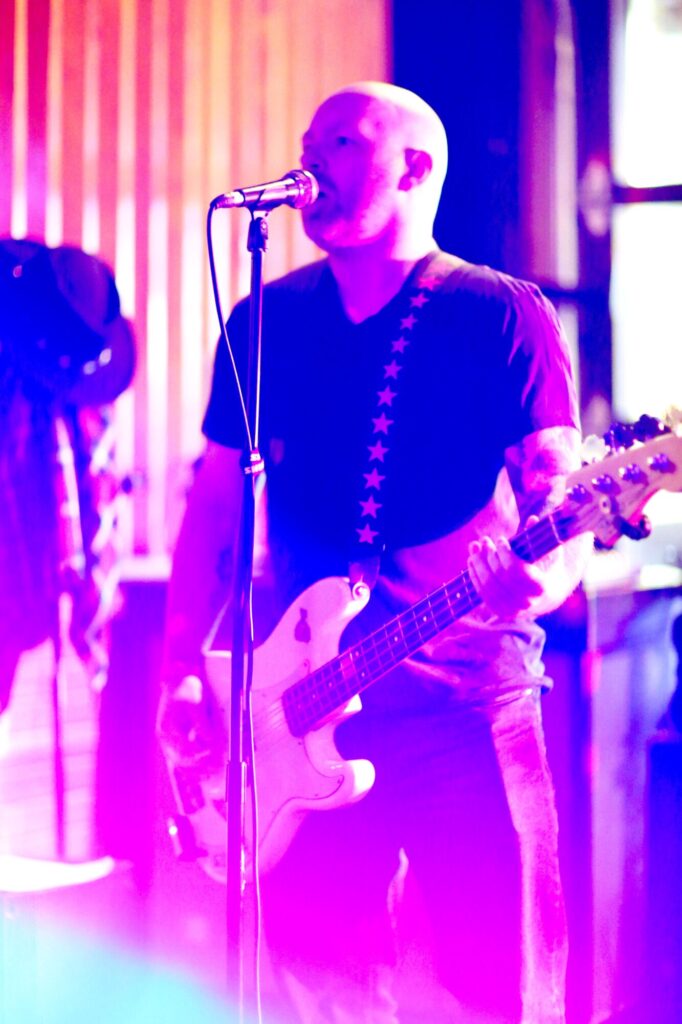 Photo of a performer playing guitar and singing onstage, while bathed in purple stage lights, during February 2025's Long Weekend Band Crawl in Waterloo, Ontario.