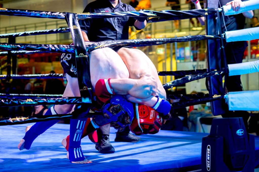 Photo taken inside the Galt Arena Gardens during Fight Night 2 of two fighters engaged in a clinch while bent over and tucked in between the ropes at the edge of the ring.