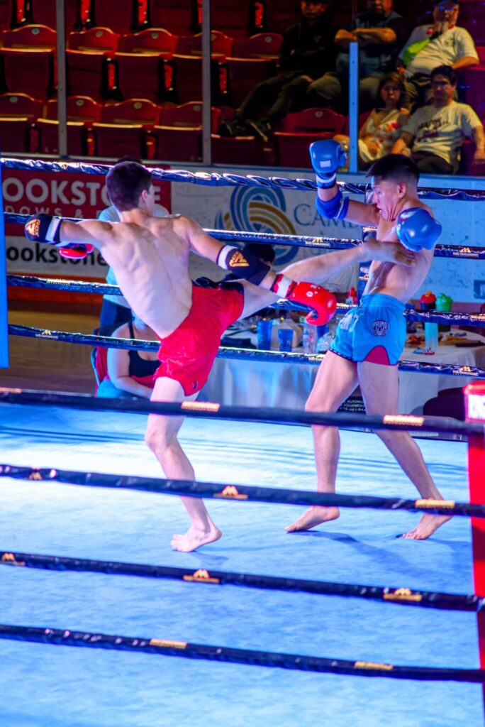 Photo taken inside the Galt Arena Gardens during Fight Night 2 of two fighters during a match, where one fighter is mid chest kick while the other recoils with his gloves up.