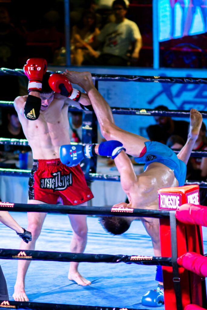 Photo taken inside the Galt Arena Gardens during Fight Night 2 of two fighters during a match, where one covers his head to shield from the other fighter's spinning handstand kick.