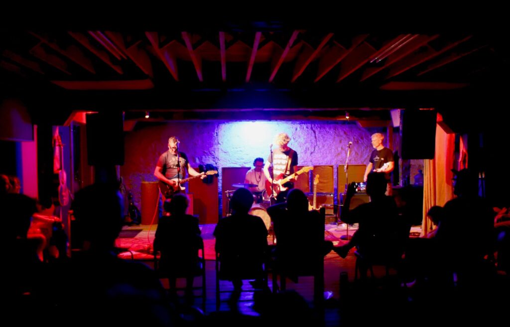 Photo taken inside of the band Spool performing inside a purple-lit hall to an audience in Kitchener, Ontario.