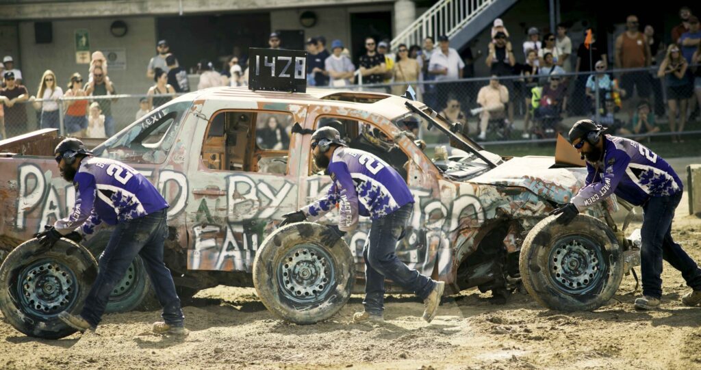 Photo of a pit crew for a derby car simultaneously rolling tires in tandem on their way to maintenance a car in Kitchener, Waterloo.