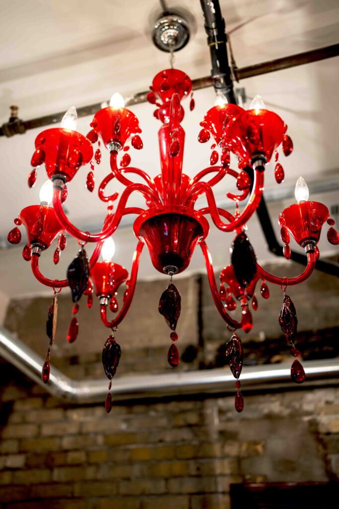 Photo of a red glass chandelier adorned with glass vagainas hanging on the ceiling of the Yoni Mudra Art Gallery in Kitchener, Ontario.